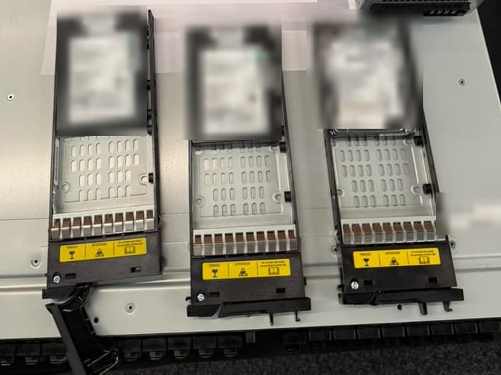 Three drive carriers pulled part-way out of a storage enclosure, showing the empty carriers and the drives above them.