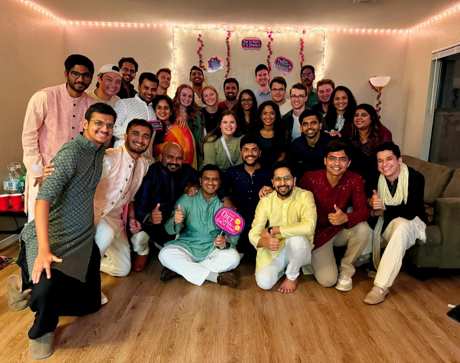 About twenty-five people in festive Indian clothing packed into a decorated apartment for a Diwali party.