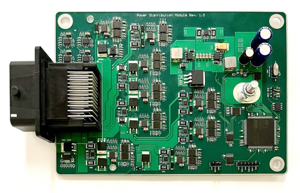 A green printed circuit board on white, silkscreened “Power Distribution Module Rev. 1.0”, with an automotive connector, microcontroller, capacitors and labeled nets for fan, fuel pump, start, ignition, ECU and dash.