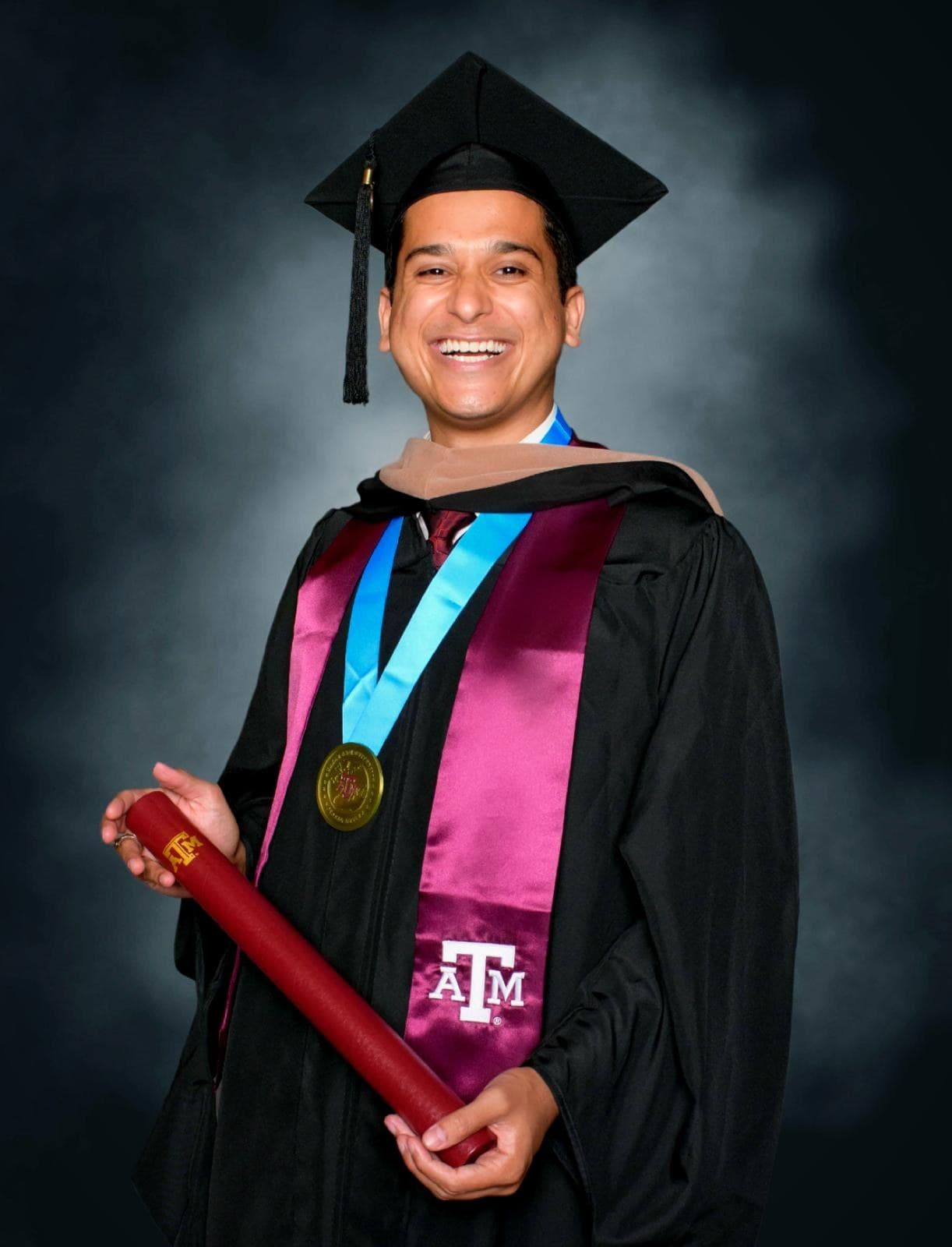 Kushagra Goyal in Texas A&M graduation regalia, holding a diploma tube.
